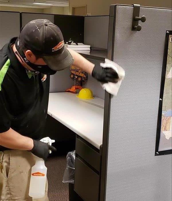 technician wearing black gloves wiping down side of office cubicle with a cleaning cloth
