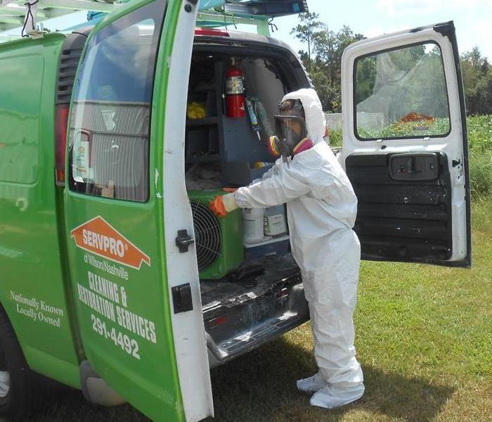 Technician wearing personal protective gear grabbing equipment from the back of a SERVPRO van